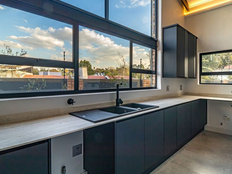 Modern kitchen featuring sleek dark cabinetry, stone countertops, a double sink with black fixtures, and large windows providing ample natural light.