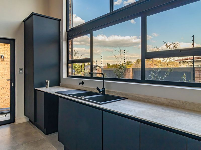 Modern kitchen featuring sleek dark cabinetry, stone countertops, a double basin sink with black fixtures, and expansive windows providing ample natural light.
