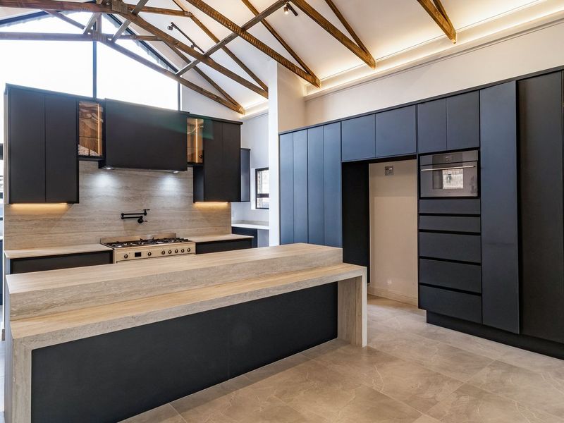 Modern kitchen featuring dark cabinetry, stone countertops, gas cooktop, built-in oven, and striking exposed timber roof trusses in a spacious, high-ceiling layout.