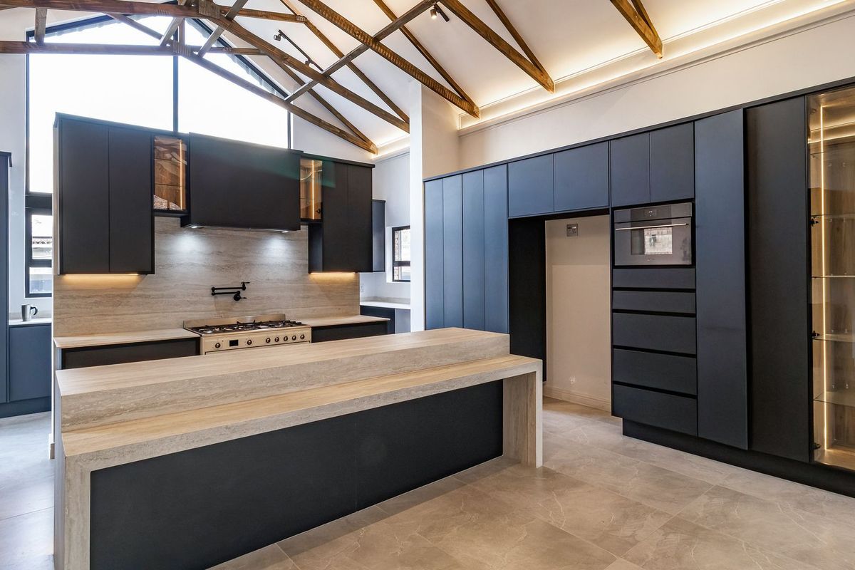 Modern kitchen featuring dark cabinetry, stone countertops, gas cooktop, built-in oven, and striking exposed timber roof trusses in a spacious, high-ceiling layout.