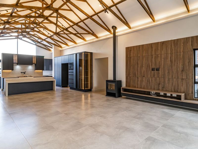 Spacious open-plan living and kitchen area featuring high vaulted ceilings with exposed timber trusses, modern dark cabinetry, and a sleek freestanding fireplace.