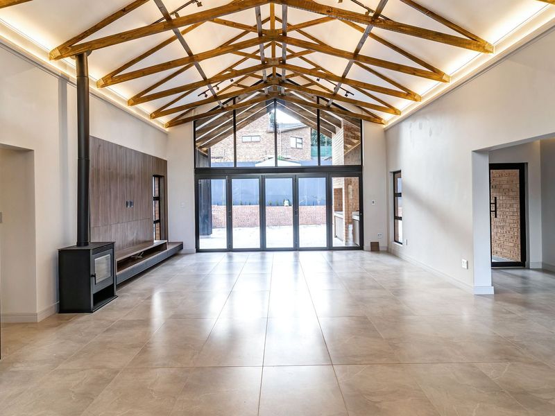 Spacious living area featuring high vaulted ceilings with exposed timber trusses, large format floor tiles, a modern fireplace, and expansive bi-fold doors to the patio.