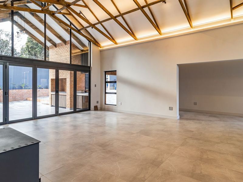 Spacious open-plan living area featuring high vaulted ceilings with exposed timber trusses, large stacker doors, and a modern freestanding fireplace.