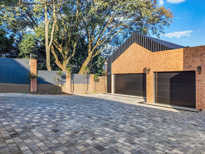 Modern brick-faced double garage with a paved driveway and secure boundary walling featuring electric fencing.