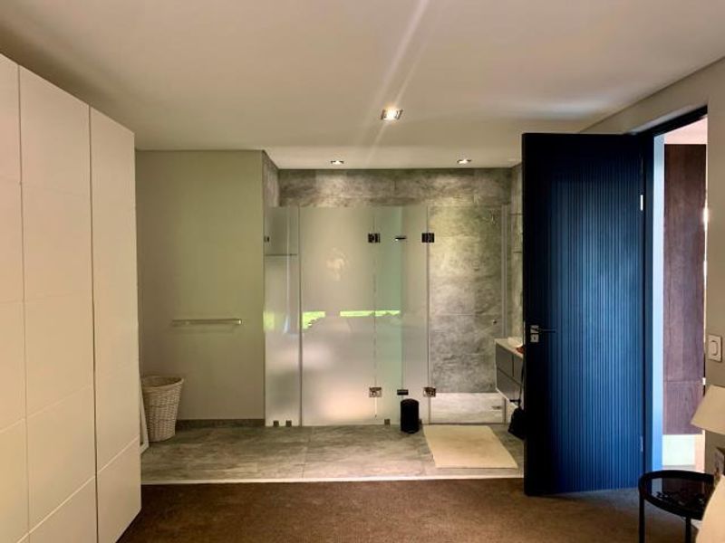 Modern bathroom featuring a glass-enclosed shower, stone-look tiling, and a sleek vanity, adjacent to a bedroom with built-in cabinetry.