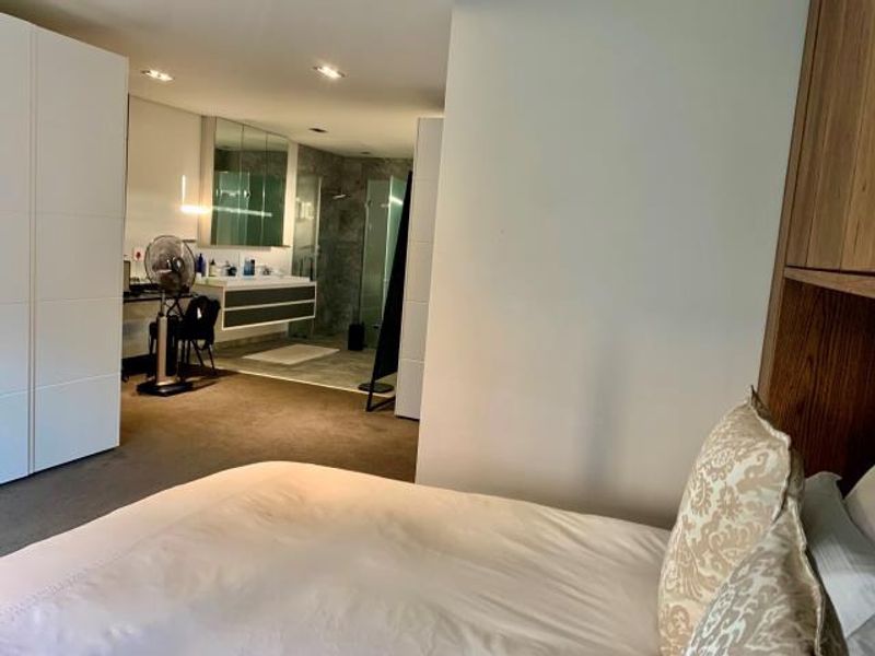 Spacious bedroom featuring integrated built-in cupboards and an open-plan en-suite bathroom with a modern floating vanity and glass-enclosed shower.