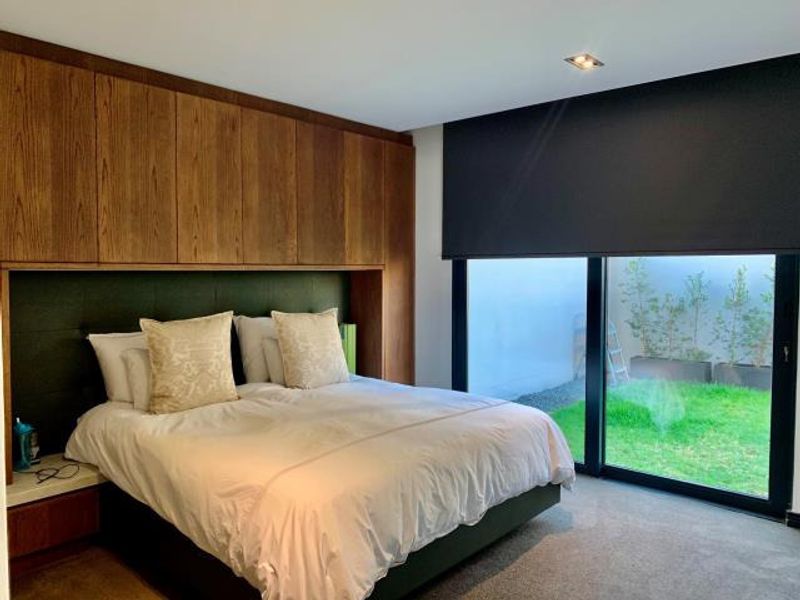 Modern bedroom featuring extensive built-in wooden cabinetry, recessed lighting, and large sliding glass doors providing direct access to a private garden area.
