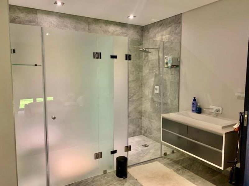 Modern bathroom featuring a spacious walk-in shower with glass enclosure, contemporary wall-mounted vanity with integrated basin, and stylish grey porcelain tiling.