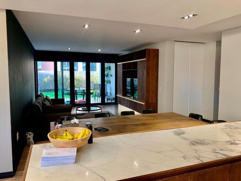 Modern open-plan living area featuring a marble kitchen island, built-in wooden cabinetry, and large sliding glass doors leading to an outdoor patio.
