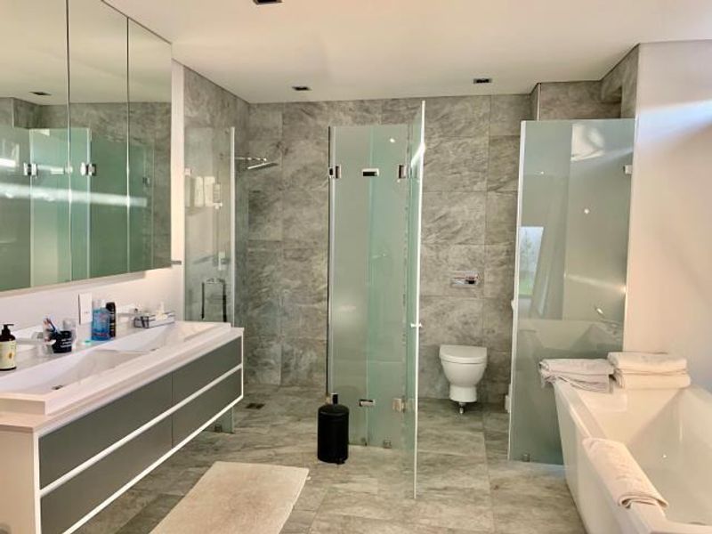 Modern bathroom featuring a double vanity, glass-enclosed shower, wall-mounted toilet, and a freestanding bathtub with high-quality stone tiling throughout.