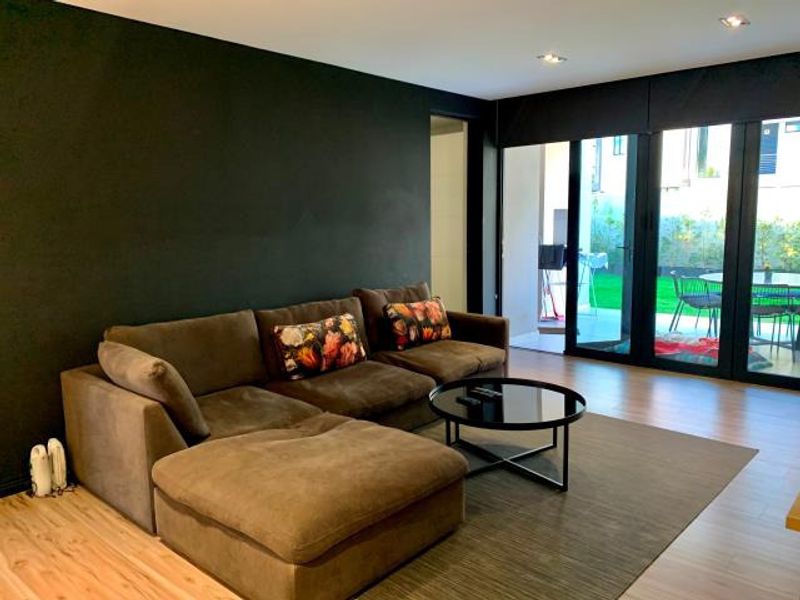 Modern living room featuring laminate flooring, recessed downlighting, and large black aluminium sliding doors providing seamless access to the outdoor patio area.