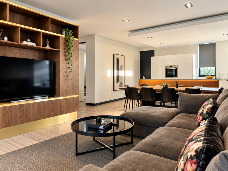 Modern open-plan living and dining area featuring a custom wooden media unit, integrated kitchen appliances, and high-quality finishes throughout.