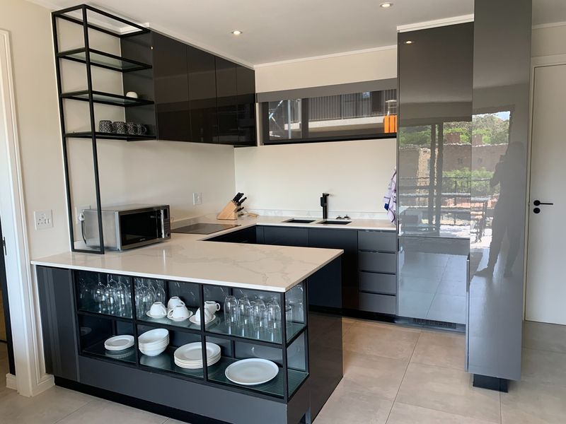 Modern kitchen featuring high-gloss cabinetry, stone countertops, integrated shelving, and premium black fixtures, offering a sleek and functional culinary space.