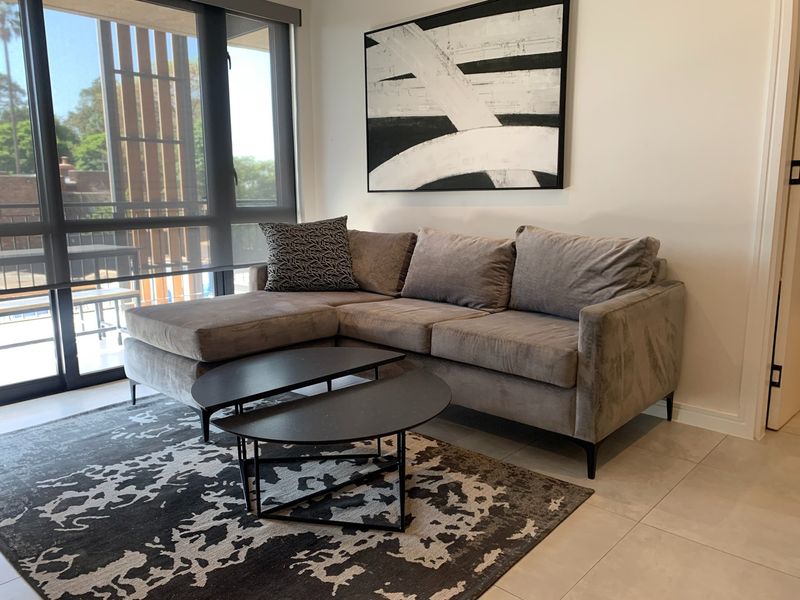A bright living room featuring large floor-to-ceiling windows with access to an outdoor area and neutral tiled flooring.