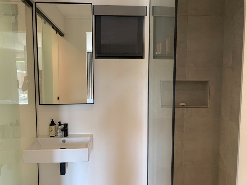 Modern bathroom featuring a wall-mounted basin with black tapware, a framed mirror, and a tiled shower enclosure with a built-in niche.