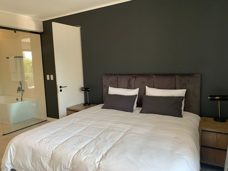 Modern bedroom featuring a dark accent wall and an integrated glass-enclosed ensuite bathroom with a freestanding bathtub.