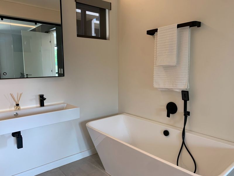 Modern bathroom featuring a sleek freestanding bathtub, wall-mounted basin with matte black fixtures, and a contemporary framed mirror.