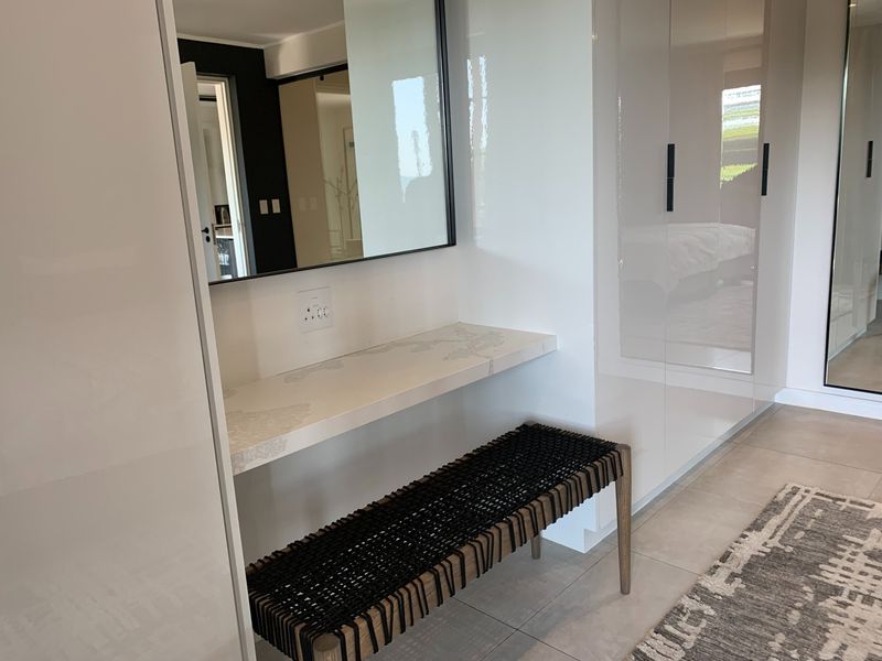 Modern bedroom area featuring high-gloss built-in cupboards, a sleek floating vanity shelf, and a wall-mounted mirror with neutral tiled flooring.