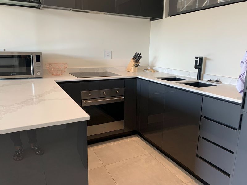 Modern kitchen featuring sleek dark glossy cabinetry, white quartz countertops, integrated oven, electric hob, and a contemporary double sink with a matte black faucet.