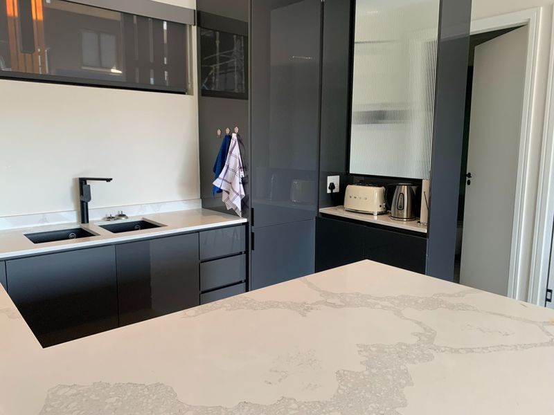 Modern kitchen featuring sleek dark cabinetry, high-quality quartz countertops, a double undermount sink with a black mixer tap, and elegant fluted glass detailing.