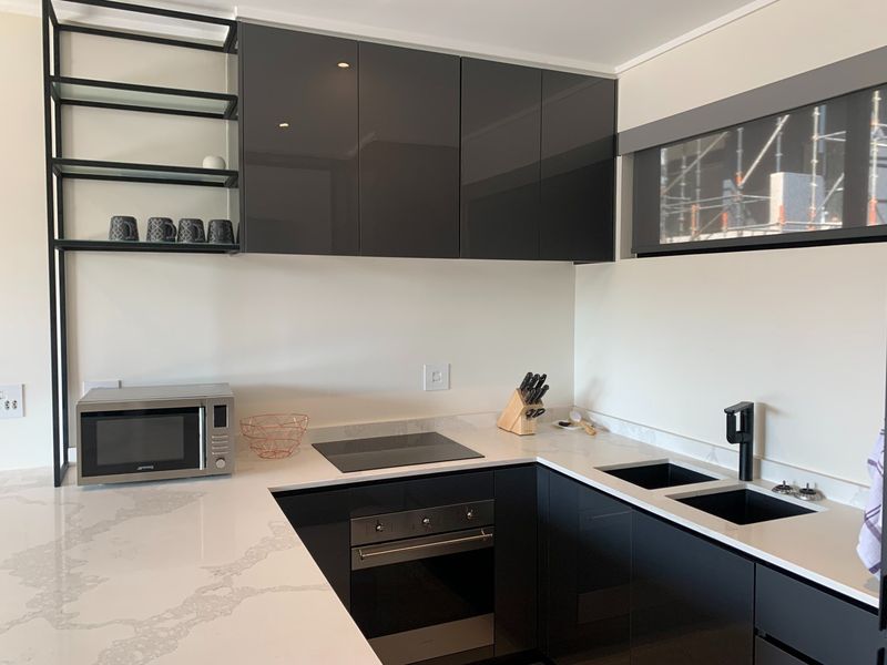 Modern kitchen featuring high-gloss cabinetry, stone countertops, integrated oven, electric hob, and a sleek black sink fixture.