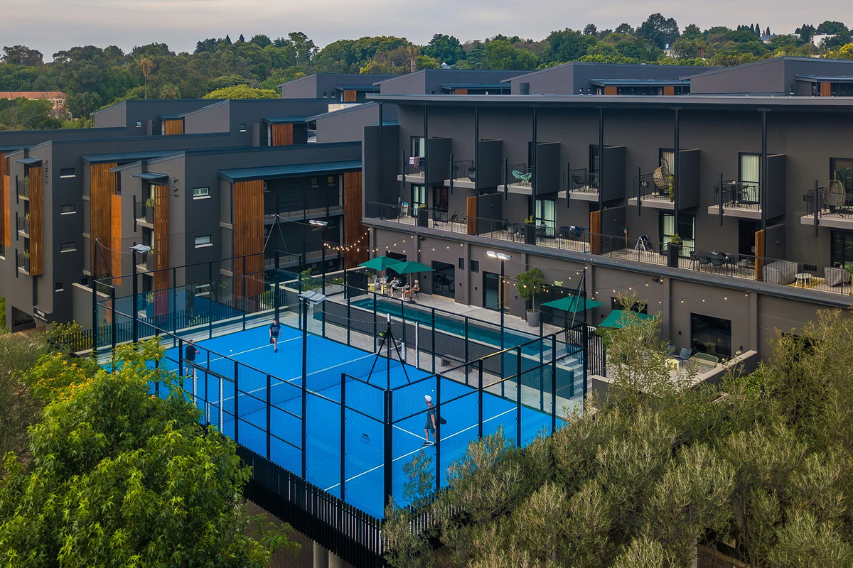 Aerial view of a modern apartment complex featuring a dedicated padel court, swimming pool, and private balconies for residents.