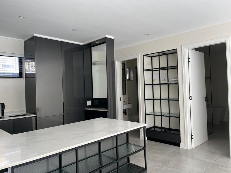 Modern kitchen featuring high-gloss cabinetry, a large quartz-topped island, and sleek tiled flooring, offering a clean and contemporary aesthetic.