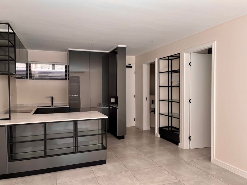 A modern, minimalist kitchen featuring sleek grey cabinetry, stone countertops, and integrated shelving, finished with neutral floor tiles and recessed lighting.