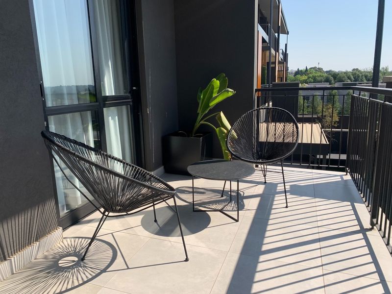 A modern apartment balcony featuring tiled flooring, a secure metal balustrade, and access via a large sliding glass door.