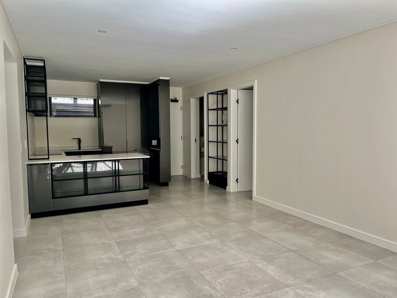 Modern open-plan living area featuring sleek grey kitchen cabinetry, stone countertops, tiled flooring, and recessed lighting in a clean, minimalist space.