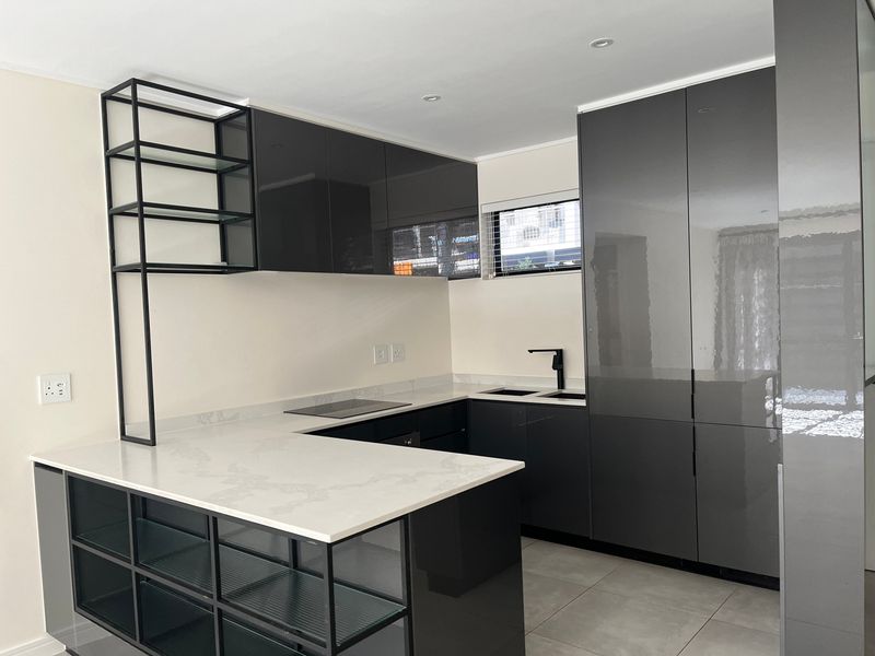 Modern kitchen featuring high-gloss dark cabinetry, white quartz countertops, integrated hob, and sleek black fixtures in a clean, contemporary layout.