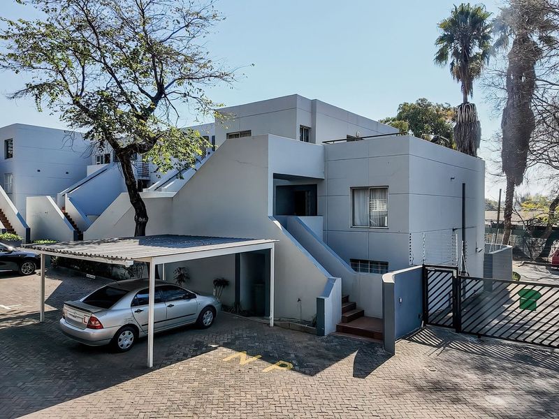 Exterior view of an apartment complex featuring a paved driveway, covered carport parking, and secure gated access with perimeter electric fencing.