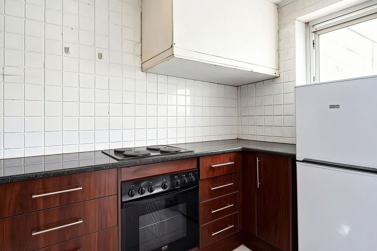 A compact kitchen featuring dark wood-finish cabinetry, granite countertops, a built-in oven with hob, and a tiled backsplash.