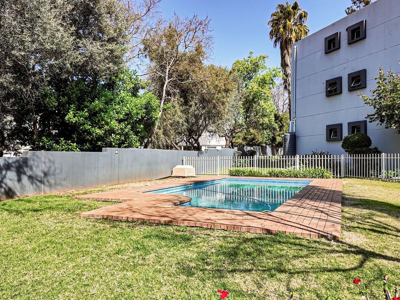 A well-maintained outdoor swimming pool area featuring brick coping, a surrounding lawn, and secure perimeter fencing.