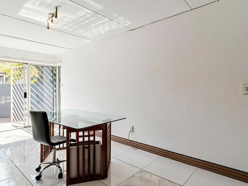 A bright office space featuring white walls, polished tile flooring, and a sliding glass door providing access to an outdoor area.