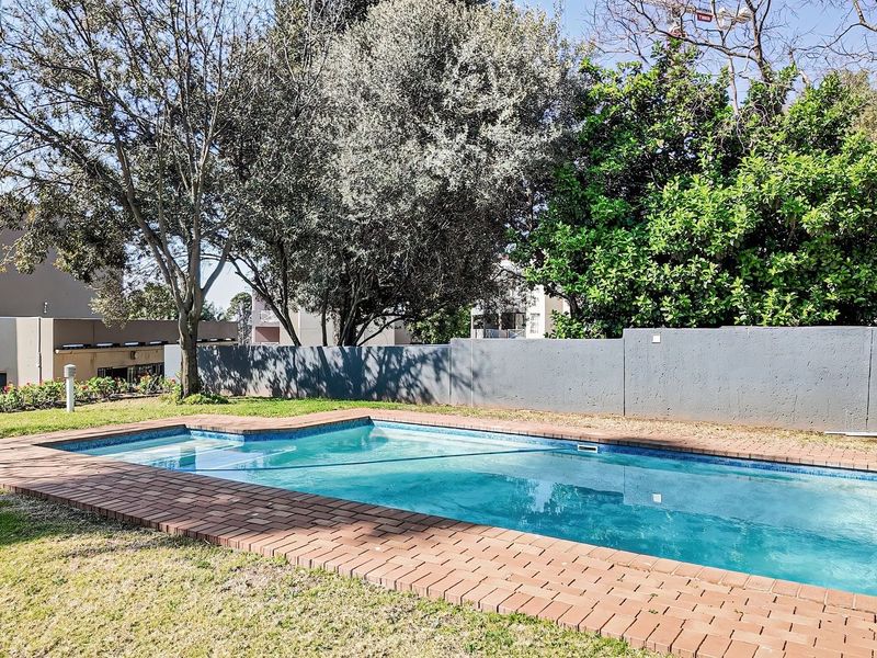 A private swimming pool area featuring brick coping, surrounded by a lawn and a boundary wall in a residential apartment complex setting.