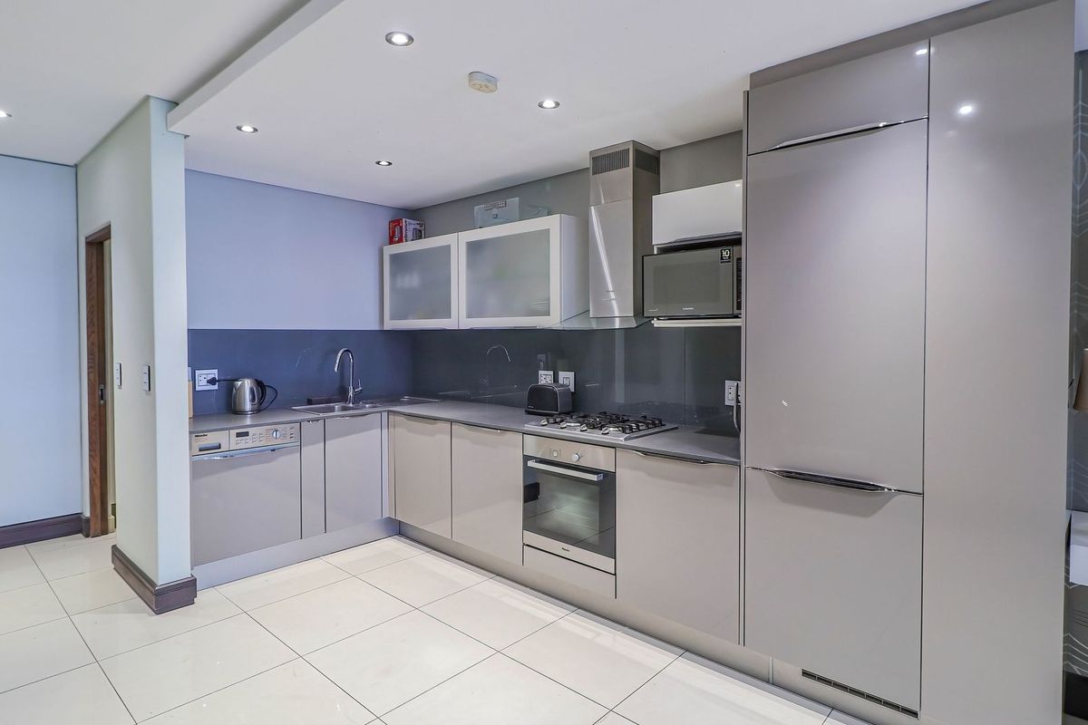 Modern kitchen featuring high-gloss cabinetry, integrated appliances, gas hob, stainless steel oven, and sleek tiled flooring in an open-plan layout.