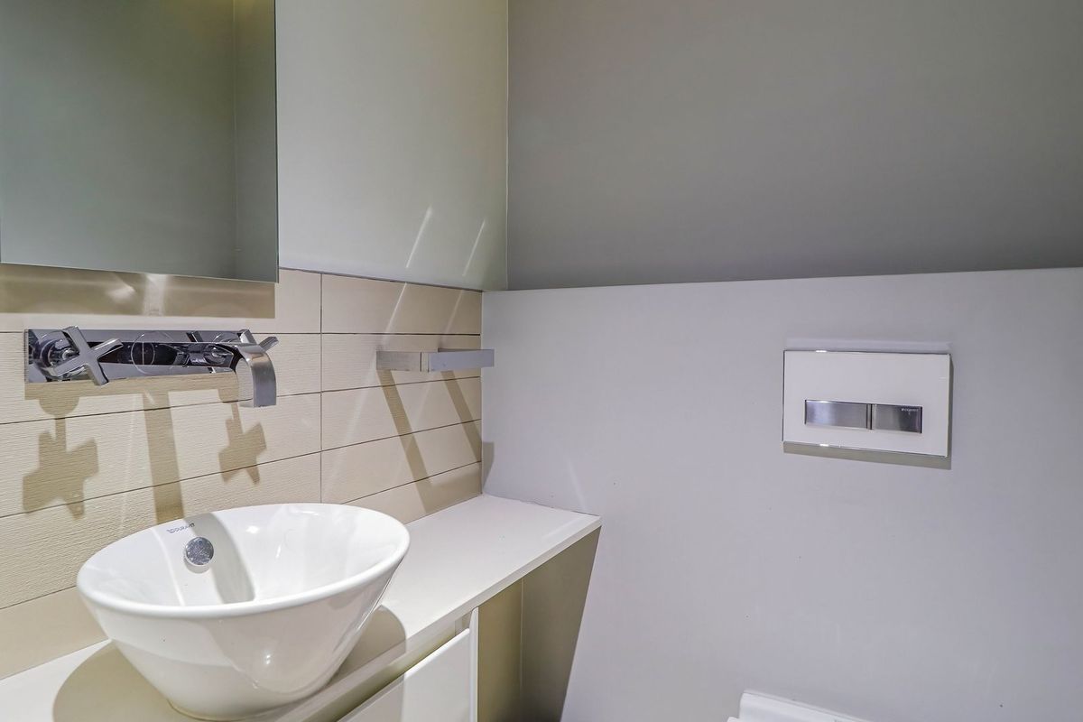 A modern bathroom featuring a sleek wall-mounted basin, chrome wall-mounted faucet, and a concealed cistern flush plate with a clean tiled splashback.