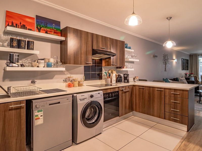 Modern open-plan kitchen featuring wood-finish cabinetry, integrated appliances, and tiled flooring, seamlessly flowing into the adjacent living and dining area.