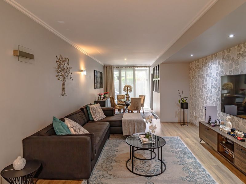Spacious open-plan living and dining area featuring modern laminate flooring, recessed lighting, and a decorative feature wall, leading to a bright patio access point.