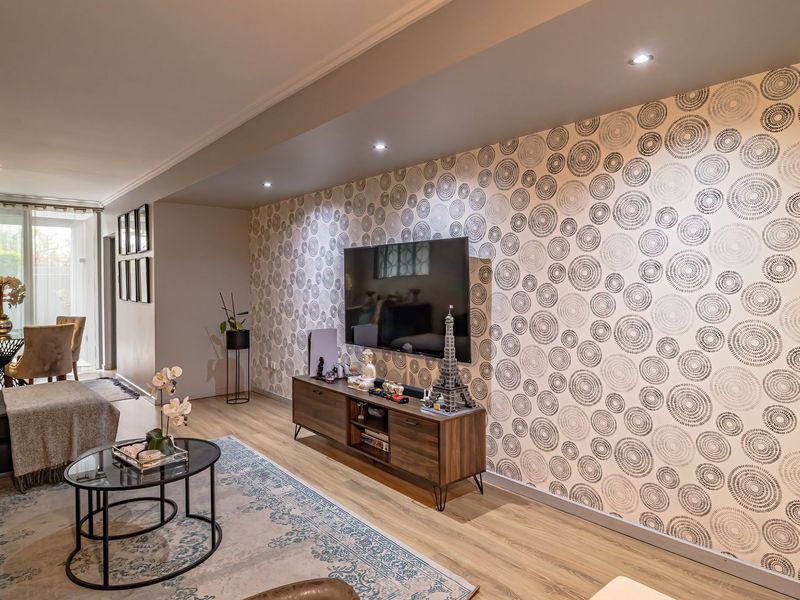 A well-maintained living room featuring modern laminate flooring, recessed downlighting, and a distinctive patterned feature wall.