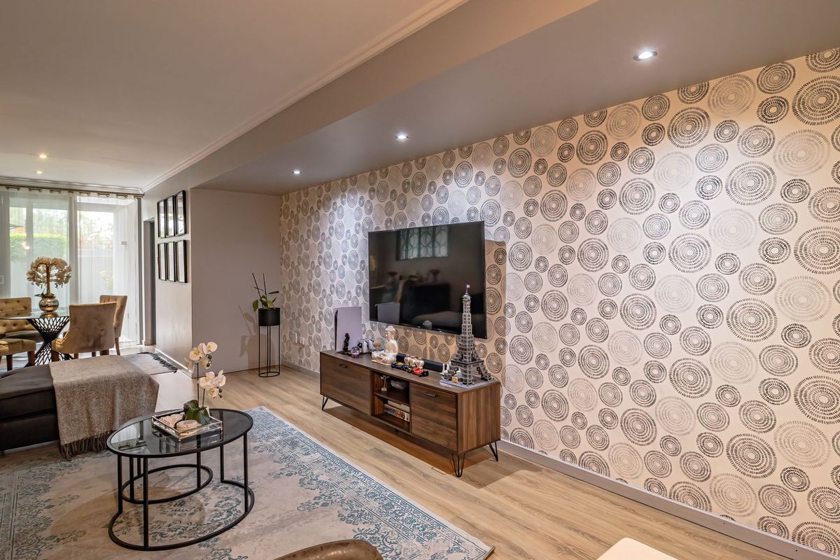 A well-maintained living room featuring modern laminate flooring, recessed downlighting, and a distinctive patterned feature wall.