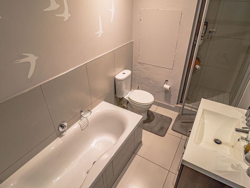 A functional bathroom featuring a built-in bathtub, separate shower enclosure, vanity with integrated basin, and neutral wall and floor tiling.