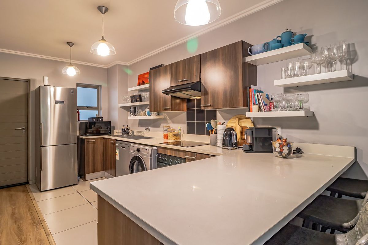 Modern kitchen featuring dark wood cabinetry, stone countertops, integrated appliances, and floating shelves, complemented by stylish pendant lighting and tiled flooring.