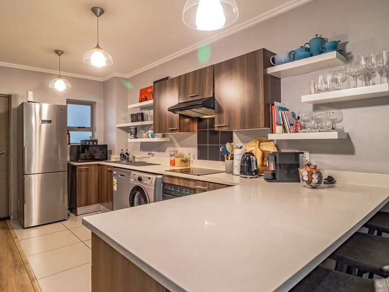 Modern kitchen featuring dark wood cabinetry, stone countertops, integrated appliances, and floating shelves, complemented by stylish pendant lighting and tiled flooring.