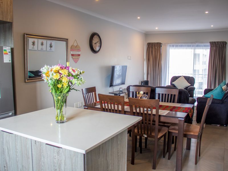 Open-plan living and dining area featuring a modern kitchen island, tiled flooring, and direct access to a balcony through sliding glass doors.