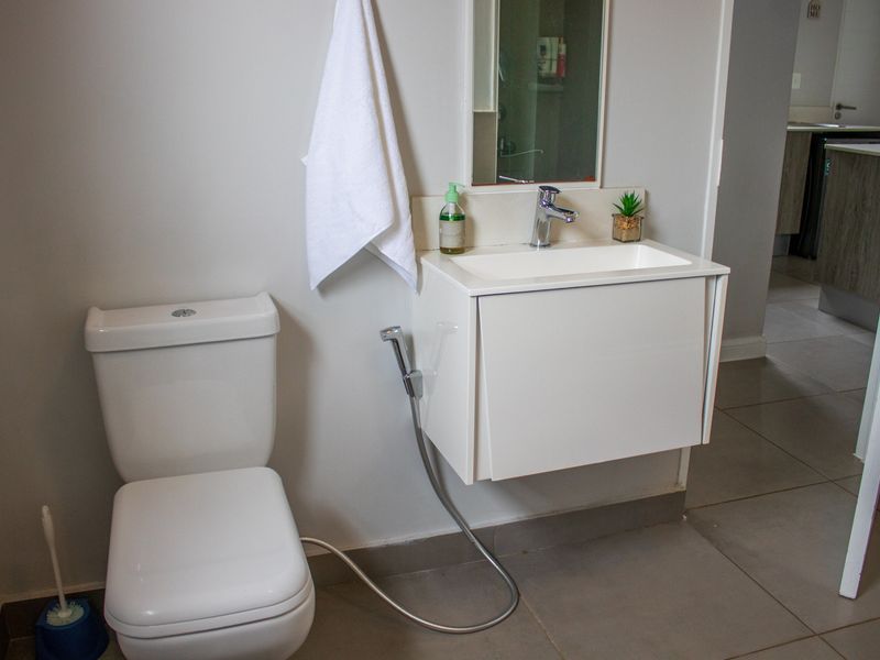 A modern bathroom featuring a wall-mounted vanity with a ceramic basin, chrome mixer tap, toilet, and bidet spray, finished with neutral floor tiles.