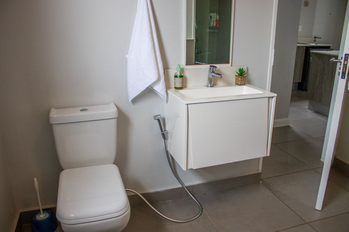 A modern bathroom featuring a wall-mounted vanity with a ceramic basin, chrome mixer tap, toilet, and bidet spray, finished with neutral floor tiles.