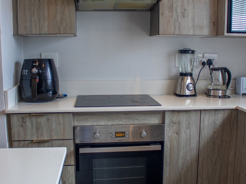 Modern kitchen featuring wood-look cabinetry, stone-look countertops, and integrated stainless steel appliances including an oven, cooktop, and extractor fan.