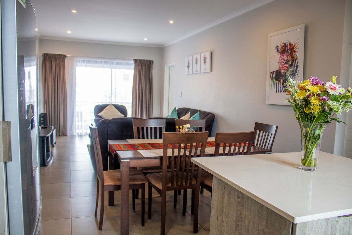 An open-plan living and dining area featuring tiled flooring, recessed lighting, and a kitchen island, leading to a balcony through sliding glass doors.